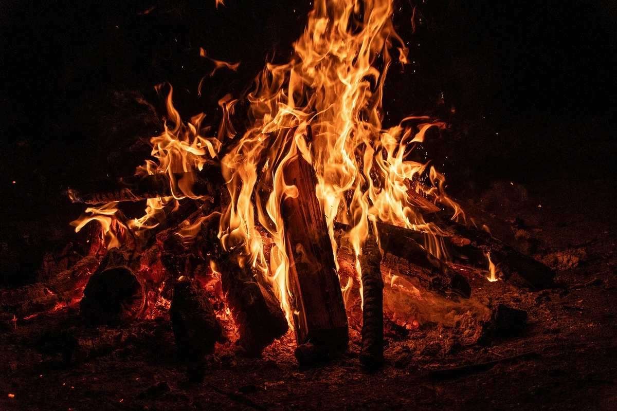 Feu de camp ardent la nuit avec flammes orangées intenses sur bois Feu de camp ardent la nuit avec flammes orangées intenses sur bois
