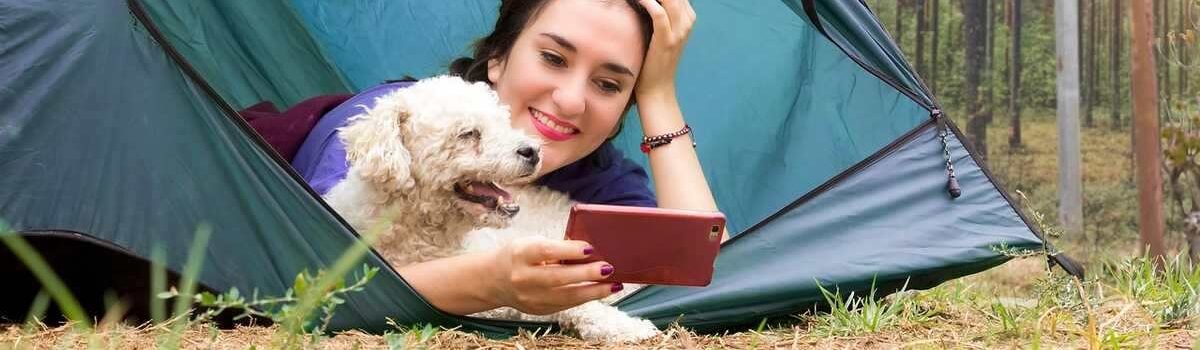 Femme allongée dans une tente bleue avec un petit chien beige, forêt en arrière-plan