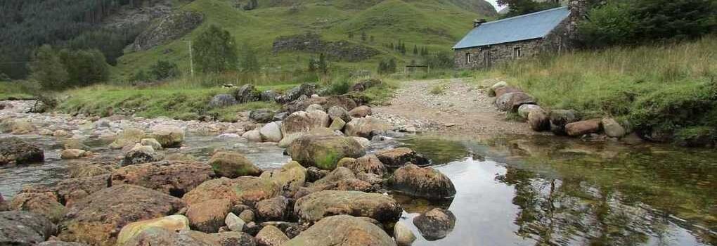 Vallée montagnarde avec ruisseau, rochers, cabane et pentes boisées