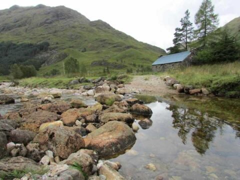 Vallée montagnarde avec ruisseau, rochers, cabane et pentes boisées