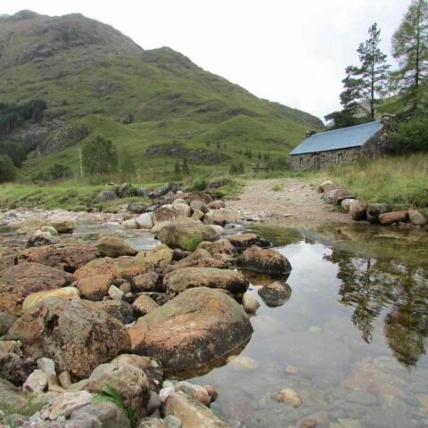 Vallée montagnarde avec ruisseau, rochers, cabane et pentes boisées