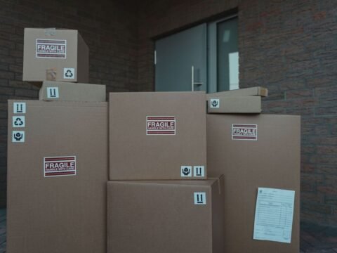 Piles de cartons FRAGILE empilés devant une porte d'un bâtiment en brique