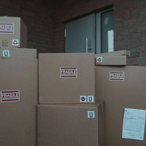 Piles de cartons FRAGILE empilés devant une porte d'un bâtiment en brique