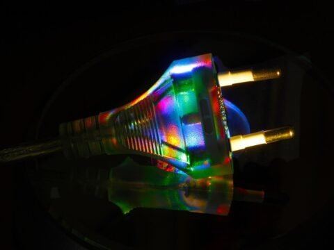 Une prise électrique illuminée par des reflets multicolores sur un fond noir