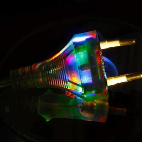 Une prise électrique illuminée par des reflets multicolores sur un fond noir