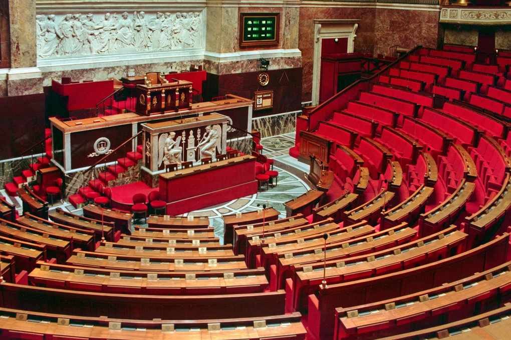 Salle parlementaire vide avec sièges en bois, bureaux et décorations sculptées