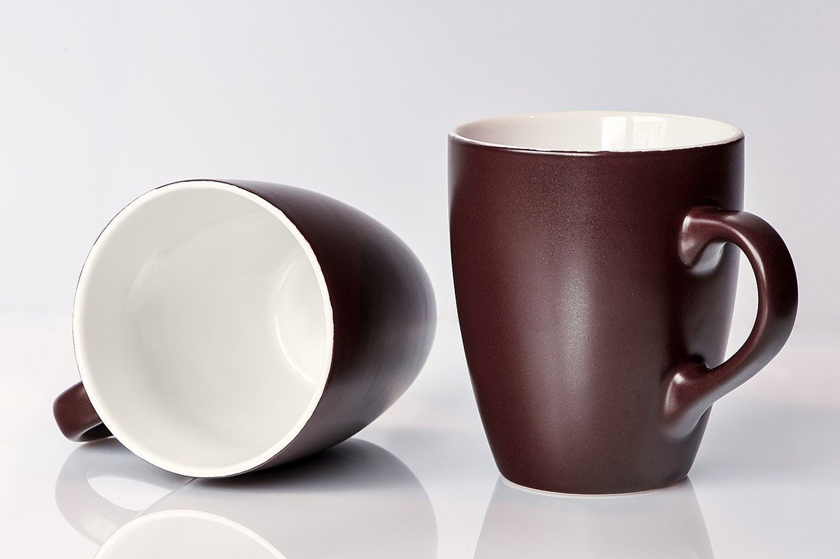 Deux tasses en céramique, une droite, une renversée, sur une surface blanche