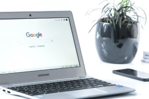 Laptop Samsung avec Google sur l'écran, smartphone et plante en pot noir à proximité