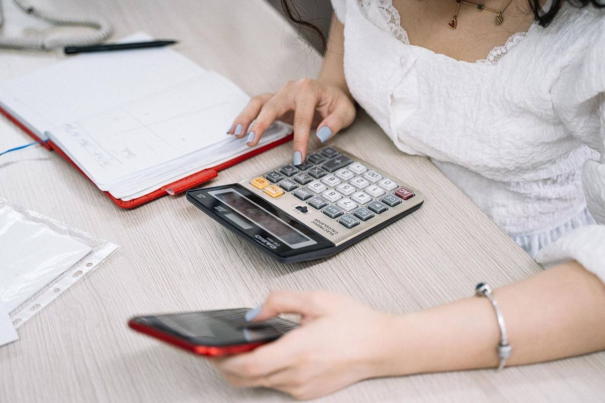 Femme manipulant une calculatrice et un smartphone sur une table de bureau Femme manipulant une calculatrice et un smartphone sur une table de bureau