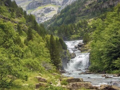 Cascade et rivière dans une vallée alpine boisée entre hautes montagnes