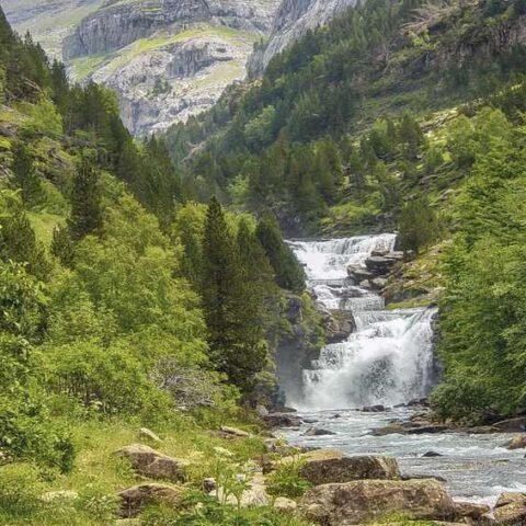 Cascade et rivière dans une vallée alpine boisée entre hautes montagnes