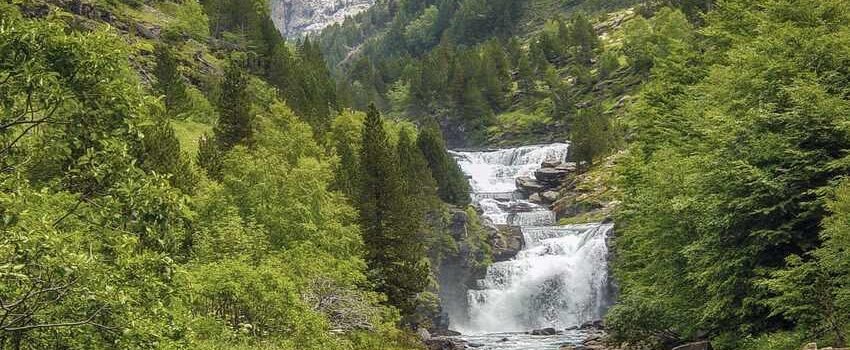 Cascade et rivière dans une vallée alpine boisée entre hautes montagnes