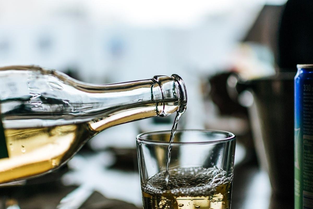 Eau dorée versée d'une bouteille dans un verre, fond flou Eau dorée versée d'une bouteille dans un verre, fond flou