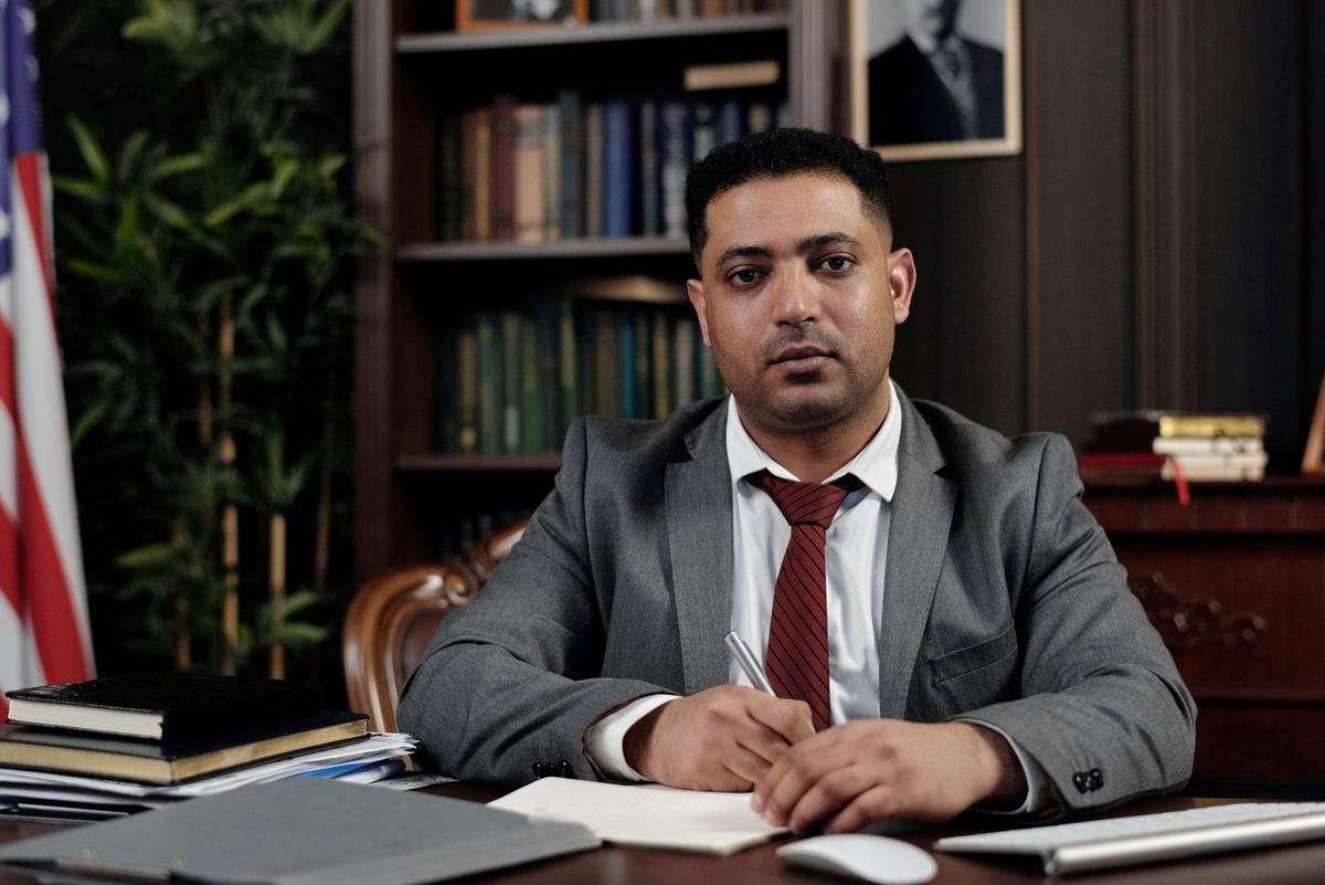 Homme écrivant à un bureau dans un bureau avec des livres et un drapeau Homme écrivant à un bureau dans un bureau avec des livres et un drapeau