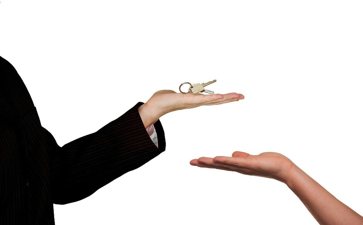 Deux mains se font face, l'une tenant une clé dorée avec anneau, symbolisant la transmission d'une propriété Deux mains se font face, l'une tenant une clé dorée avec anneau, symbolisant la transmission d'une propriété