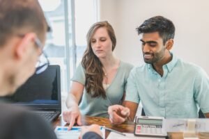 Trois individus en réunion avec ordinateur et documents sur un bureau
