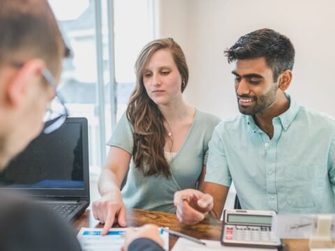 Trois individus en réunion avec ordinateur et documents sur un bureau