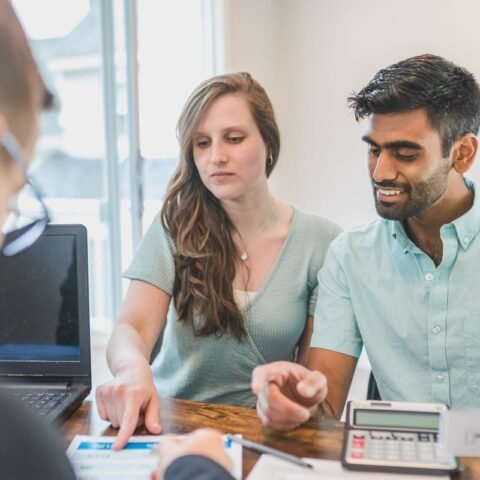 Trois individus en réunion avec ordinateur et documents sur un bureau