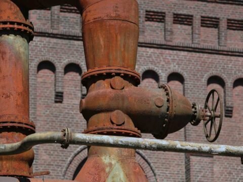 Pipes rouillés et vanne à main devant un mur de brique