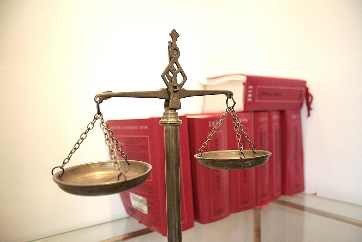 Balance de justice en bronze sur une table devant des livres rouges reliés Balance de justice en bronze sur une table devant des livres rouges reliés