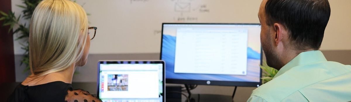 Deux collaborateurs assis à un bureau regardent ensemble un ordinateur portable et un écran de bureau