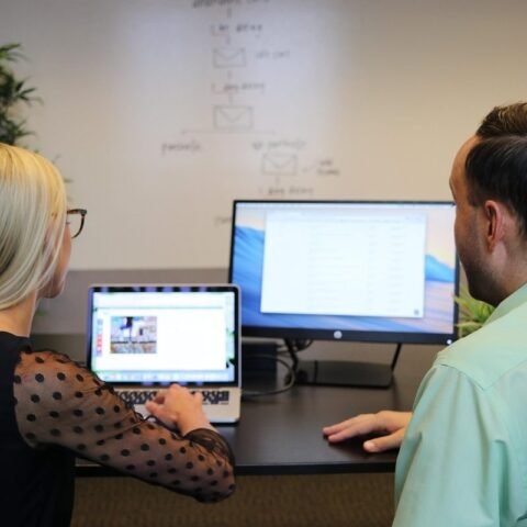 Deux collaborateurs assis à un bureau regardent ensemble un ordinateur portable et un écran de bureau