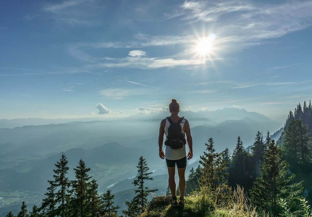 Une randonneuse solitaire admire le soleil au-dessus des montagnes et forêts