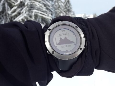 Montre connectée montrant une montagne sur son écran, portée sur un bras ganté