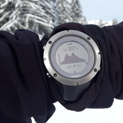 Montre connectée montrant une montagne sur son écran, portée sur un bras ganté