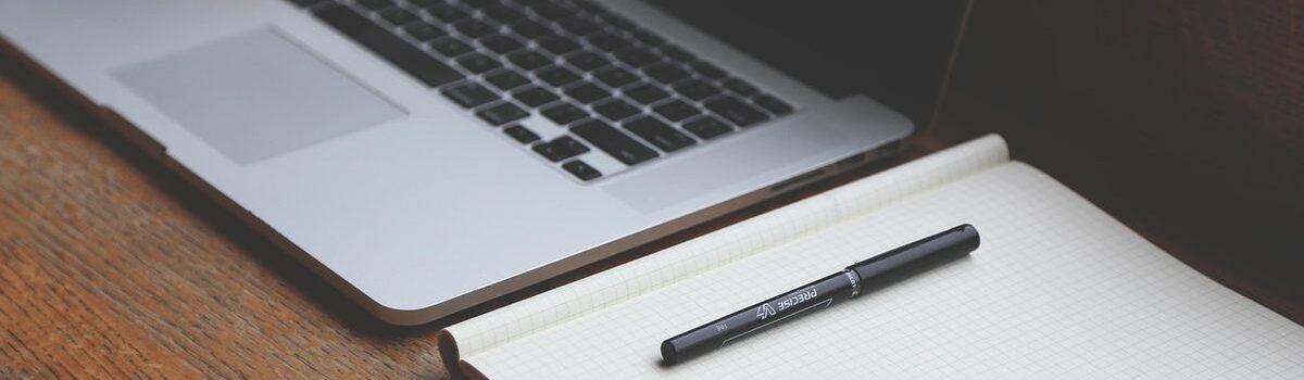 Un ordinateur ouvert, un cahier vierge et un stylo sur du bois
