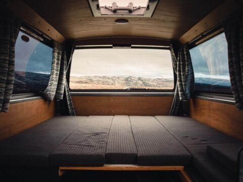 Intérieur d'un véhicule camper avec lit pliant, rideaux et vue extérieure