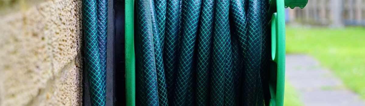 Un tuyau vert enroulé sur un support vert, fixé à un mur extérieur