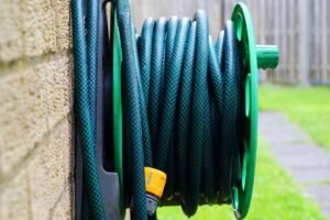 Un tuyau vert enroulé sur un support vert, fixé à un mur extérieur