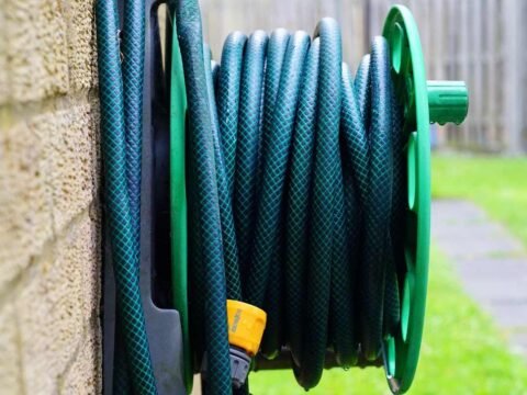 Un tuyau vert enroulé sur un support vert, fixé à un mur extérieur