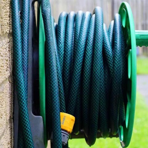 Un tuyau vert enroulé sur un support vert, fixé à un mur extérieur