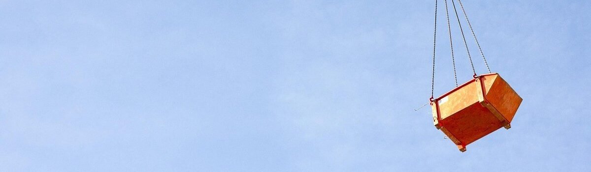 Un caisson orange suspendu par des câbles à une grue dans le ciel