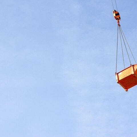 Un caisson orange suspendu par des câbles à une grue dans le ciel